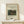 May include: Framed art print in light wood frame showing Henri Rousseau's jungle painting with lion attacking antelope amid lush green foliage. Print has cream background with black text identifying the 1905 artwork. Displayed on light wooden surface with small white wrapped gift box beside it against neutral wall.