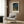 May include: Framed Japanese woodblock print showing foxes gathered under a bare tree at night with blue sky, displayed on wood paneled wall above beige upholstered armchair with geometric patterned pillow, brass floor lamp and dark round side table with open book nearby