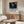 May include: Japanese woodblock print style poster featuring a large hawk with detailed feathers flying over a snowy landscape with mountains and water under a deep blue starry sky, displayed in light wood frame above mid-century modern walnut credenza in minimalist room setting with white curved chair, glass coffee table, and warm natural lighting