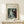 May include: Framed art print of Renoir's impressionist painting showing a woman in a flowing white dress playing piano, displayed on light wood console table with small wrapped gift beside it. The reproduction features soft brushstrokes in blues, whites and earth tones within a thin wooden frame against cream walls.