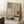 May include: Japanese-inspired artwork in natural wood frame leaning against white wall. Features minimalist composition with red sun, delicate pine branches, geometric black lines, and green rectangular element on neutral beige background. Styled room scene with white coffee cup on wooden block and cream textured rug.