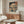 May include: Japanese woodblock print artwork displayed in modern living room setting, featuring snow-covered mountain landscape with traditional buildings and blue water. Framed print hangs above wooden sideboard with glass top coffee table, white upholstered chair, and minimalist floor lamp. Cream walls and natural lighting create serene, contemporary interior design aesthetic.
