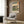 May include: Japanese woodblock print artwork in white frame on wood wall, featuring Mount Fuji landscape with green trees and traditional scenery in blue, green, and cream tones. Shown above modern beige armchair with geometric patterned pillow, beside brass floor lamp and dark side table with open book.