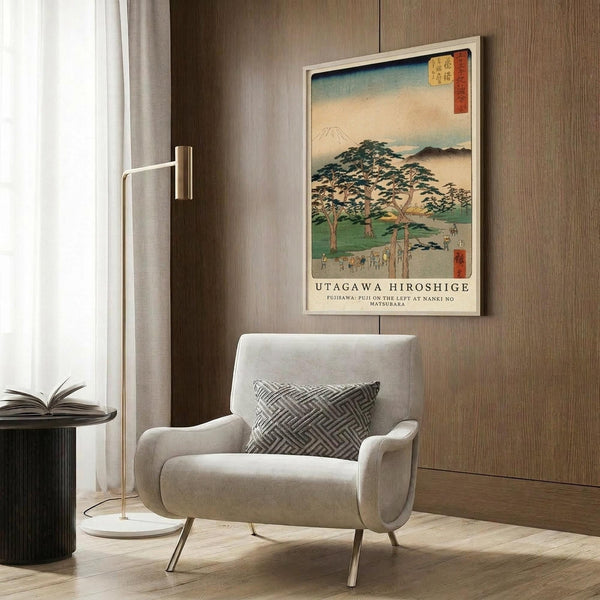May include: Japanese woodblock print artwork in white frame on wood wall, featuring Mount Fuji landscape with green trees and traditional scenery in blue, green, and cream tones. Shown above modern beige armchair with geometric patterned pillow, beside brass floor lamp and dark side table with open book.