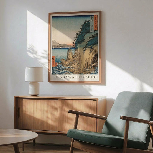 May include: Japanese woodblock print artwork showing coastal landscape with rocky cliffs, blue water, and Mount Fuji in distance, displayed in wooden frame above mid-century modern credenza with ceramic lamp, next to sage green upholstered chair with wooden arms in sunlit room with white walls
