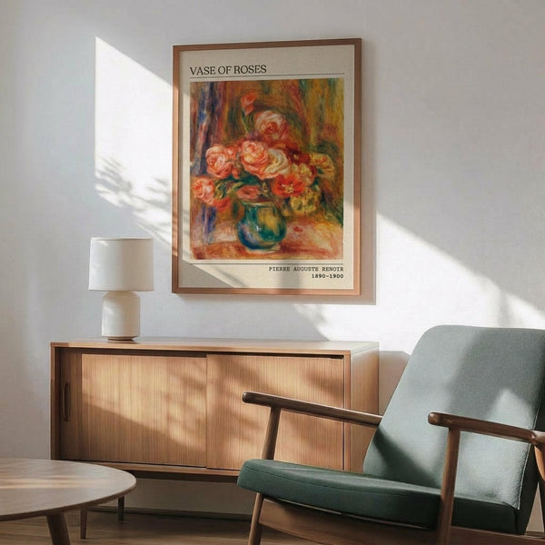May include: Framed art print of impressionist roses in blue vase hanging on white wall above wooden sideboard. Mint green mid-century armchair with wooden arms sits nearby. Warm sunlight creates diagonal shadows across the modern living room scene. The colorful floral painting features soft brushstrokes in pink, coral, and green tones with cream matting and thin brown frame.