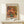 May include: Framed art print of an impressionist painting showing pink and coral roses in a blue-green vase, displayed on a light wood console table with a small white wrapped gift. The poster features warm, painterly brushstrokes in a gold frame against a cream wall.