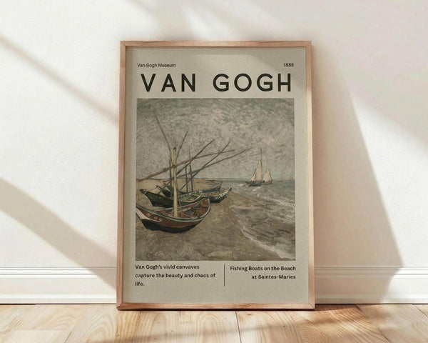 May include: Framed Van Gogh museum poster displaying fishing boats on a beach scene from 1888, featuring muted earth tones and the artist's characteristic brushwork. The beige and cream colored print shows boats with masts on sandy shore with waves, presented in natural wood frame leaning against white wall on light wooden floor with soft window lighting.