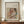 May include: Framed art print displaying Renoir's soft pastel painting of a woman in white dress tenderly holding a small child in coral clothing, with cream matting and brown frame, positioned on wooden sideboard alongside white ceramic vase and stacked books against elegant paneled wall
