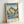 May include: Framed Japanese woodblock print showing dramatic coastal cliffs in yellow and green hues with blue water below, featuring traditional ukiyo-e art style with Japanese text in red cartouches, displayed in light wooden frame leaning against white wall