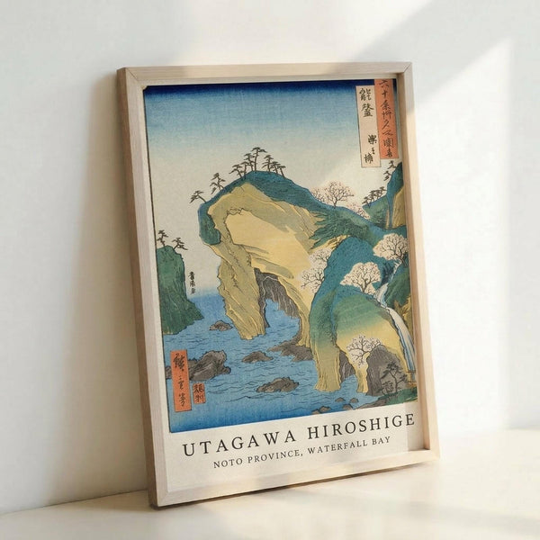 May include: Framed Japanese woodblock print showing dramatic coastal cliffs in yellow and green hues with blue water below, featuring traditional ukiyo-e art style with Japanese text in red cartouches, displayed in light wooden frame leaning against white wall