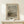 May include: Framed Van Gogh museum poster featuring fishing boats on a beach in muted earth tones, displayed on a light wood console table beside a small wrapped gift with twine and greenery sprig against a cream wall