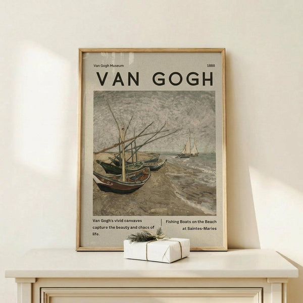 May include: Framed Van Gogh museum poster featuring fishing boats on a beach in muted earth tones, displayed on a light wood console table beside a small wrapped gift with twine and greenery sprig against a cream wall