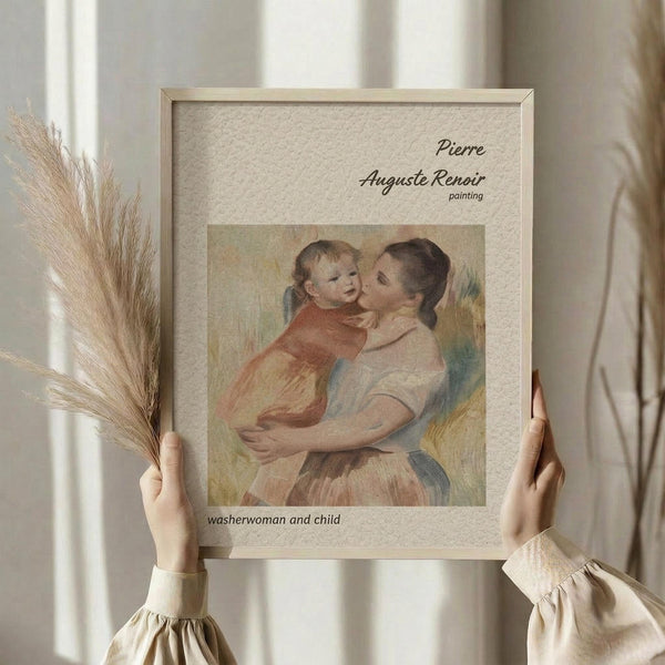 May include: Person in cream ruffled sleeves holding framed reproduction of Renoir's impressionist painting showing woman embracing young child in soft pastels. Light wood frame with beige mat, displayed against white curtained window with dried pampas grass bundle visible to left side.