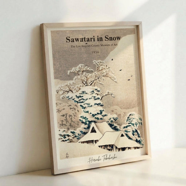 May include: Framed vintage-style Japanese woodblock print featuring snow-covered traditional houses beneath stylized blue and white waves, bare winter trees, and flying birds against a cream background. The artwork is displayed in a light wooden frame leaning against a white wall, showing muted earth tones and classic ukiyo-e aesthetic with Japanese characters visible in the corner.