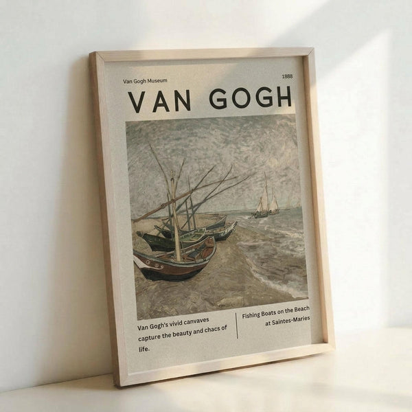 May include: Framed museum-style poster print featuring Van Gogh's 1888 painting of fishing boats on a beach. The artwork shows weathered boats with tall masts pulled up on sandy shores, with rough seas and additional boats in the background. Text reads "Van Gogh Museum 1888" at top, with descriptive text below about the artist's vivid canvases capturing life's beauty and chaos. Light wood frame sits against white wall on white surface.