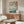 May include: Japanese woodblock print artwork showing cherry blossoms framing a lake scene with Mount Fuji in background, displayed above a mid-century modern walnut credenza in minimalist living room with cream walls, white sculptural chair, glass oval coffee table, and modern table lamp