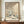 May include: Framed vintage Japanese woodblock print showing snow-covered houses with steep roofs, bare winter trees, and rolling hills in muted beige and blue tones. The artwork sits on a wooden sideboard between a round white ceramic vase and stacked books against cream wainscoted walls. Museum exhibition text and artist signature visible on the print.