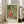 May include: Framed Japanese woodblock print featuring a monk in red robes sitting on a striped tiger, surrounded by various animals and mythological creatures on a green geometric patterned background. The print is displayed in a light wood frame leaning against a white wall next to a beige sofa in a bright, modern living room with large windows and natural lighting.