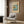 May include: Japanese woodblock print artwork displayed in modern living room with beige armchair, geometric pillow, brass floor lamp, and dark wood paneling. The framed poster shows a coastal scene with rocky outcrops, blue ocean waters, and traditional Japanese artistic style in muted blues, browns, and coral tones.