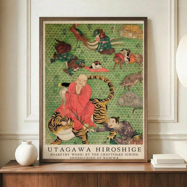 May include: A framed Japanese woodblock print reproduction displayed on a wooden sideboard against white wainscoting. The artwork features a monk in red robes seated on a tiger, surrounded by various animals and figures on a green geometric patterned background. A small white ceramic vase and stacked books sit beside the brown-framed print, which shows rich colors including orange, green, and coral tones in the traditional ukiyo-e style.