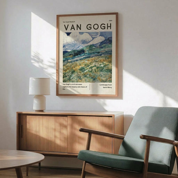 May include: Van Gogh museum poster featuring swirling wheat field landscape with cloudy blue sky and rolling green hills, displayed in light wood frame above mid-century modern credenza with white ceramic lamp, next to sage green upholstered armchair with wooden arms in sunlit room with white walls.