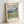 May include: Framed Van Gogh landscape poster leaning against white wall. The print features swirling brushstrokes in blues, greens, and yellows depicting rolling hills under a dramatic cloudy sky. Text reads "VAN GOGH" at top with "Van Gogh Museum 1889" and "Landscape from Saint-Rémy" below the artwork. Light wood frame surrounds cream-colored poster with museum-style layout and descriptive text about Van Gogh's vivid canvases.
