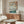 May include: Japanese woodblock print artwork displayed above wooden sideboard in modern living room. Print shows cherry blossoms framing Mount Fuji landscape with blue water, boats, and traditional architecture. Cream upholstered chair, glass coffee table, and white table lamp visible. Print appears in thin wooden frame against neutral wall.