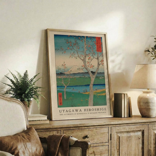 May include: Framed Japanese woodblock print reproduction featuring a cherry blossom tree with Mount Fuji in the background, displayed on a rustic wooden sideboard next to a fern plant, ceramic vase, and books in a neutral-toned living room setting with soft natural lighting.