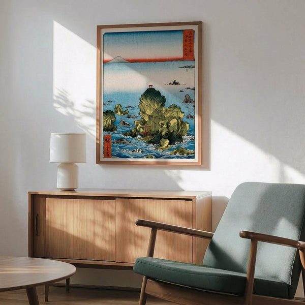 May include: Japanese woodblock print artwork displayed on white wall above wooden credenza, featuring rocky coastal landscape with small structures on cliffs, blue ocean waters, and Mount Fuji silhouette in distance under gradient sky. Print has traditional red Japanese text cartouches and warm wood frame. Scene includes mid-century modern sage green upholstered chair with wooden arms, white ceramic table lamp, and circular wood coffee table in sunlit room.