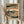 May include: Person holding framed Japanese woodblock print showing traditional landscape with buildings, people, and water in muted blues, oranges, and earth tones. Light wooden frame, displayed against white curtains with dried pampas grass visible on left side.