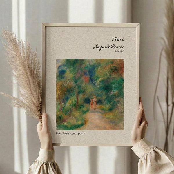May include: Person in beige clothing holding framed reproduction of Renoir's impressionist painting showing two small figures on a tree-lined path in soft greens, blues and earth tones. Light wooden frame with cream matting displays artwork title and artist name. Dried pampas grass visible beside frame against soft natural lighting.