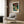 May include: Framed Japanese woodblock print featuring autumn maple trees with red foliage over a dramatic waterfall and blue water, displayed on wood paneled wall above modern beige armchair with geometric pillow. Brass floor lamp and side table with open book complete the contemporary room setting.