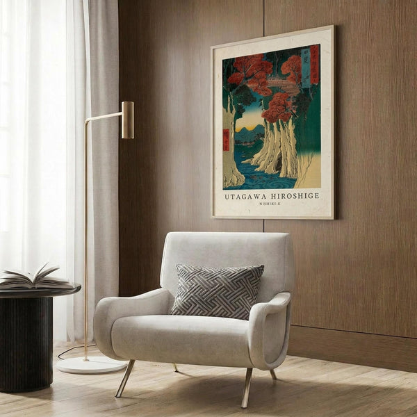 May include: Framed Japanese woodblock print featuring autumn maple trees with red foliage over a dramatic waterfall and blue water, displayed on wood paneled wall above modern beige armchair with geometric pillow. Brass floor lamp and side table with open book complete the contemporary room setting.