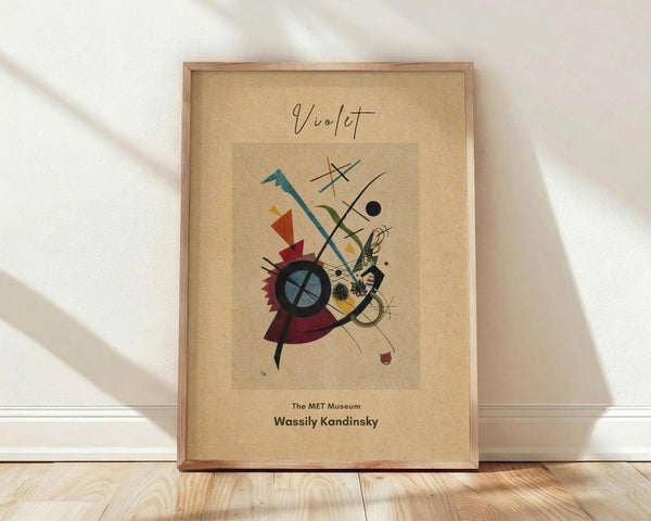 May include: Framed abstract art print featuring geometric shapes in vibrant colors including teal, red, yellow, and burgundy with black lines and circles on cream background. Wooden frame leans against white wall on light wood flooring with soft natural lighting creating diagonal shadows across the scene.