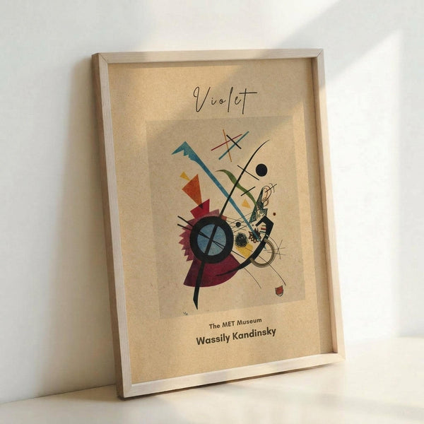 May include: Abstract art print in light wood frame leaning against white wall. Features geometric shapes, lines, and circles in blues, reds, yellows, and greens on cream background. Shows museum attribution text at bottom. Modern minimalist display setting with natural lighting creating soft shadows.