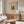 May include: Abstract Kandinsky art poster with colorful geometric shapes and lines on beige background, displayed above walnut credenza in modern living room. White curved chair and glass coffee table nearby, with brass floor lamp and white table lamp creating warm lighting on cream walls.