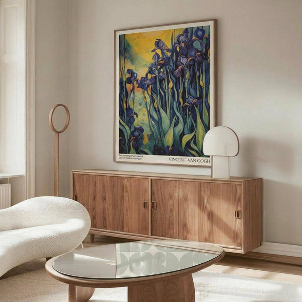 May include: Van Gogh's Irises artwork poster in thin wooden frame hanging above walnut sideboard in modern living room. Print shows purple irises with flowing green leaves against yellow background in post-impressionist style. Room features cream walls, white curved chair, glass oval coffee table, and warm wood furniture with natural lighting creating shadows.