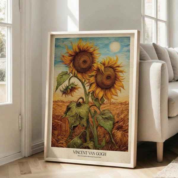 May include: Framed sunflower artwork in light wooden frame leaning against white wall next to beige upholstered chair. Print shows two large golden sunflowers with detailed petals and dark centers, green stems and leaves, set against blue sky with sun and golden wheat field below. Vintage-style poster with artist name at bottom.