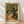 May include: Framed Van Gogh-style print showing a gnarled olive tree with swirling yellow-green foliage beside a winding dirt path leading to a small white house with red roof. The painting features thick, expressive brushstrokes in golden yellows, deep greens, and earth tones. Light wood frame rests against white wall on natural wood flooring with diagonal window shadows crossing the scene.
