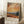 May include: Framed Van Gogh-style landscape poster with swirling orange and cream sky, rolling golden hills, dark cypress trees, and distant blue mountains. The artwork features thick, textured brushstrokes characteristic of post-impressionist painting. White matting displays artist name and inspirational quote below the image. Frame leans against white wall on fluffy cream rug beside wooden side table with white coffee cup and saucer.