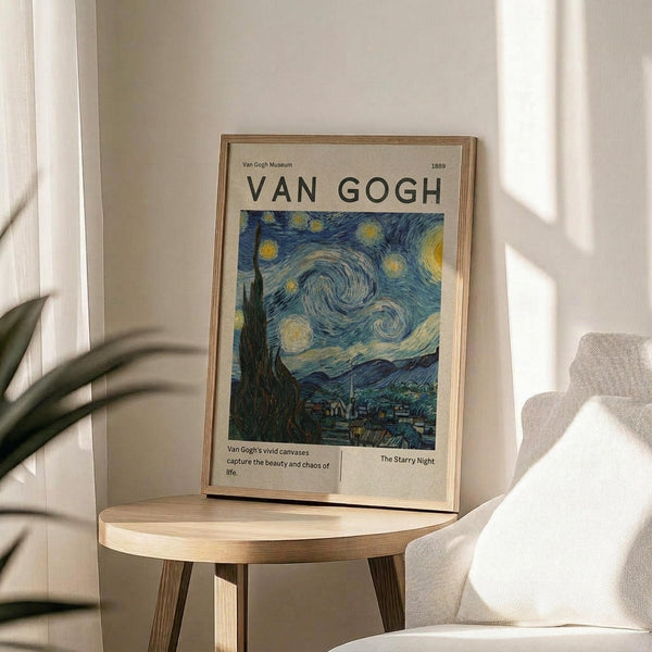 May include: Framed poster featuring Van Gogh's The Starry Night painting with swirling blue sky, yellow stars and moon, dark cypress tree, and village below. Museum-style exhibition poster with "VAN GOGH" text and "1889" date in thin wooden frame, displayed on round wooden side table next to beige upholstered chair. Soft natural lighting creates shadows on white wall, with green plant leaves visible in corner.