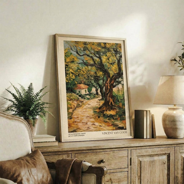 May include: Framed Van Gogh olive trees print with swirling brushstrokes in golden yellows and greens, showing a gnarled tree beside a small cottage on a cobblestone path. The artwork sits on a weathered wood sideboard next to a fern plant, table lamp, ceramic vase, and stacked books in a warm, neutral living room setting.