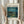 May include: Person in beige sweater holding framed Van Gogh museum poster featuring Starry Night Over the Rhone painting with swirling blue night sky, yellow stars, and water reflections. Dried wheat stalks visible on left side. Light wooden frame against neutral curtained background.