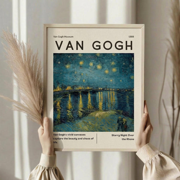 May include: Person in beige sweater holding framed Van Gogh museum poster featuring Starry Night Over the Rhone painting with swirling blue night sky, yellow stars, and water reflections. Dried wheat stalks visible on left side. Light wooden frame against neutral curtained background.