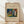 May include: Framed art print leaning against white wall on light wooden floor with natural window shadows. Features abstract expressionist painting with vibrant blues, greens, reds, and yellows in organic flowing shapes. Beige poster background with elegant script title and artist name in black text. Natural wood frame surrounds cream-colored print in minimalist room setting.