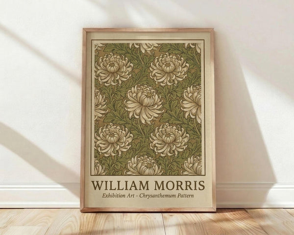 May include: Framed poster with William Morris chrysanthemum pattern in olive green and cream tones, featuring repeating floral motifs with curved petals and flowing leaves. Light wood frame with beige matting, leaning against white wall on light wooden floor with soft natural lighting creating diagonal shadows.
