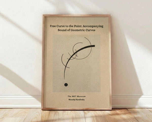 May include: Framed abstract art print leaning against white wall on light wood floor. Beige poster features black curved lines and circles in minimalist geometric design. Text reads "Free Curve to the Point: Accompanying Sound of Geometric Curves" and "The MET Museum Wassily Kandinsky" in black typography. Natural wood frame with soft window light casting diagonal shadows across white textured wall.