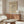 May include: Beige poster with black curved lines and text mounted above wooden sideboard in minimalist room. White sculptural chair and glass coffee table visible. Natural lighting creates soft shadows on cream walls. Modern Scandinavian-style interior with warm wood tones.