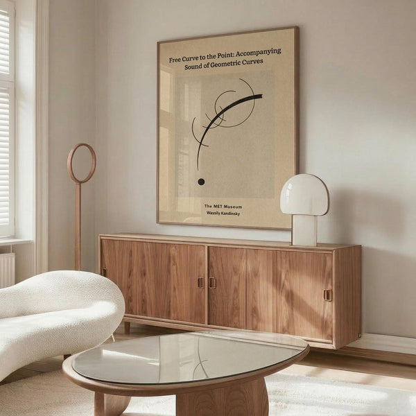May include: Beige poster with black curved lines and text mounted above wooden sideboard in minimalist room. White sculptural chair and glass coffee table visible. Natural lighting creates soft shadows on cream walls. Modern Scandinavian-style interior with warm wood tones.